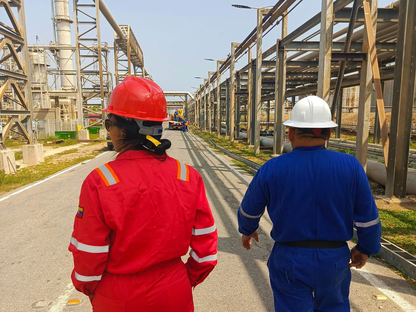 Two plant workers in hi-vis coveralls and hard hats walking through a chemicals production facility