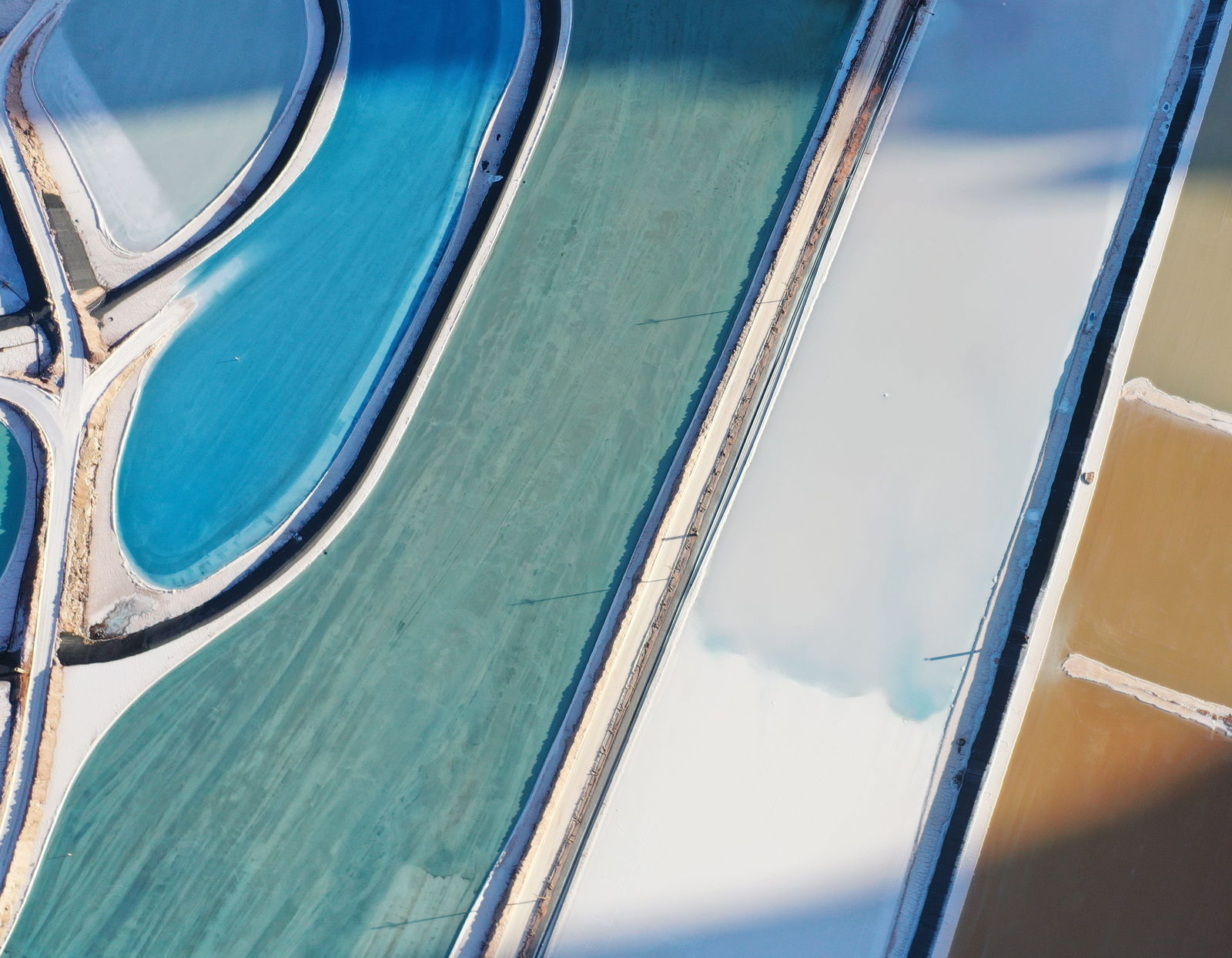 Aerial view of teal and turquoise brine evaporation ponds, where seawater is concentrated to produce marine chemicals